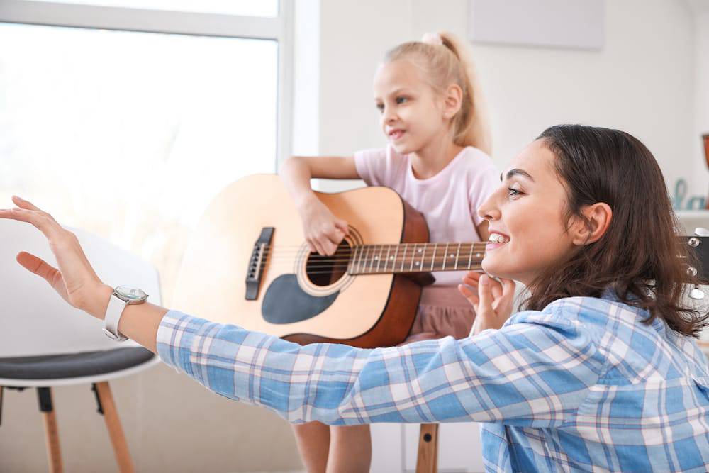 A woman teaching a little girl how to play guitar