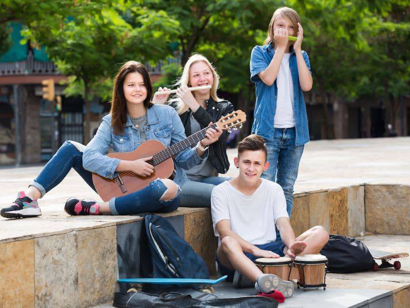 A group of teen students play music together outside