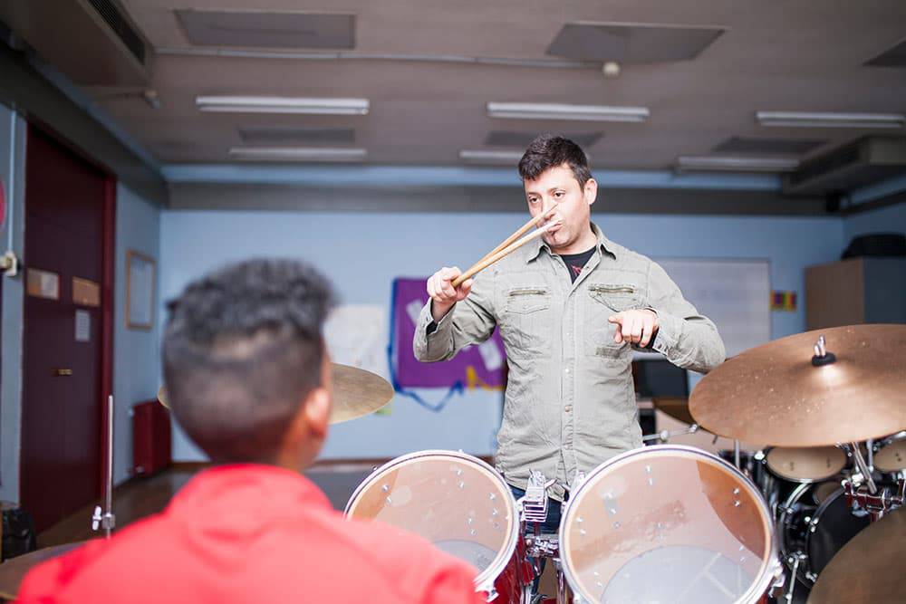 Student behind drum set with teacher in front instructing him