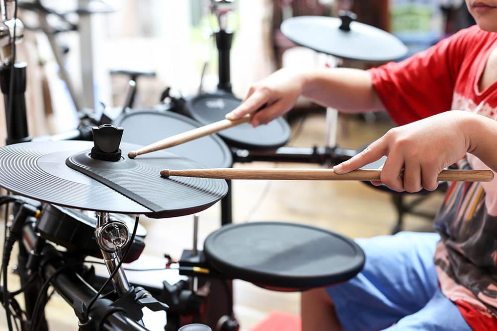 Close up of kids hands with drumsticks playing on drum set with sound pads