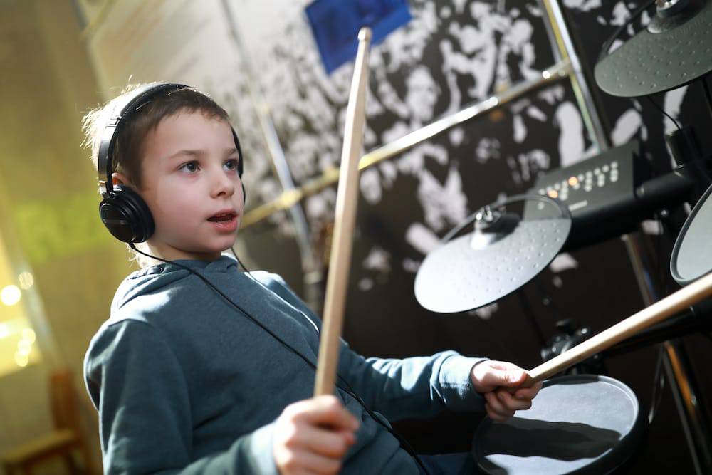 A little boy playing the drums while wearing headphones