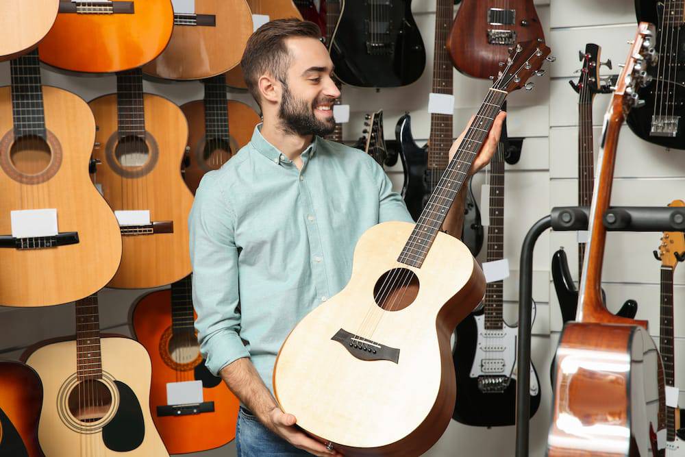 A young man looking at guitars in store prior to taking online guitar classes
