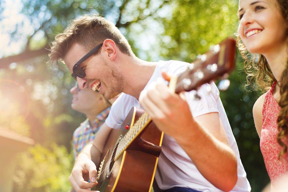 A young man plays guitar outside with his friends