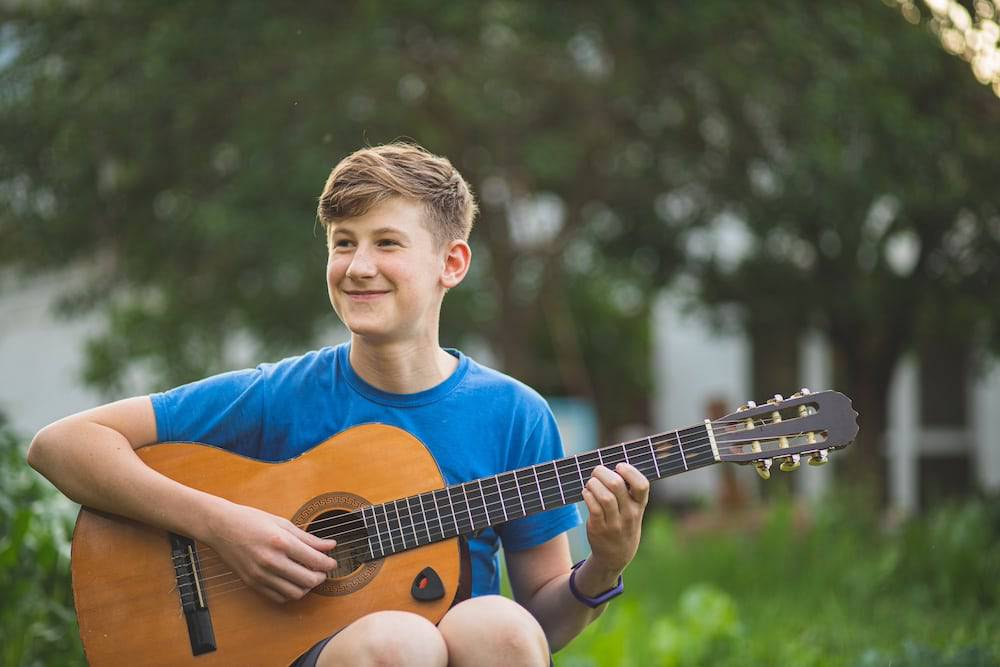 A happy teen boy plays the guitar