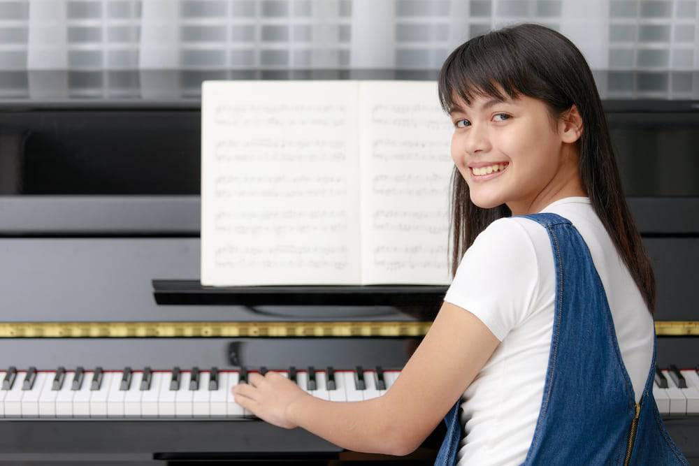 A teenage girl sits to play the piano