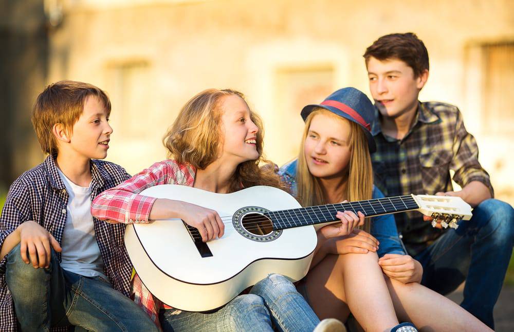 Group of teens outside playing guitar and enjoying the benefits of private music lessons