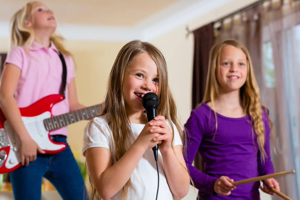Three girls practice playing and singing as they attend a music summer camp