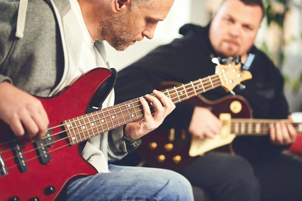 Two adult friends play their guitars together