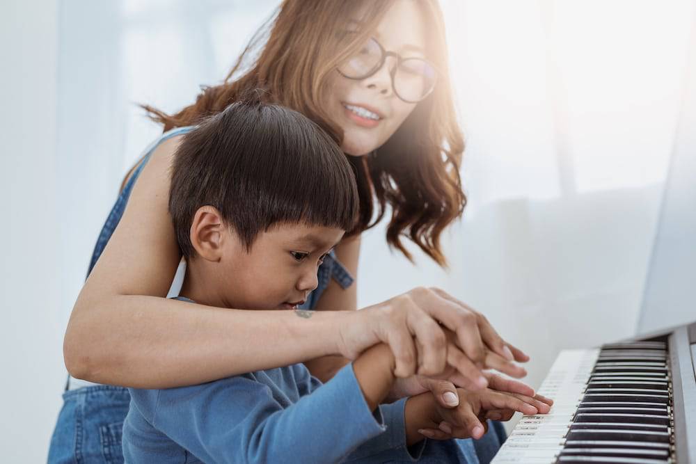 A young boy and his mother sit and play the piano together
