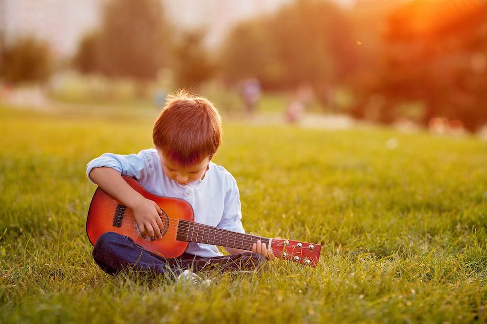 A young boy practicing his guitar outside