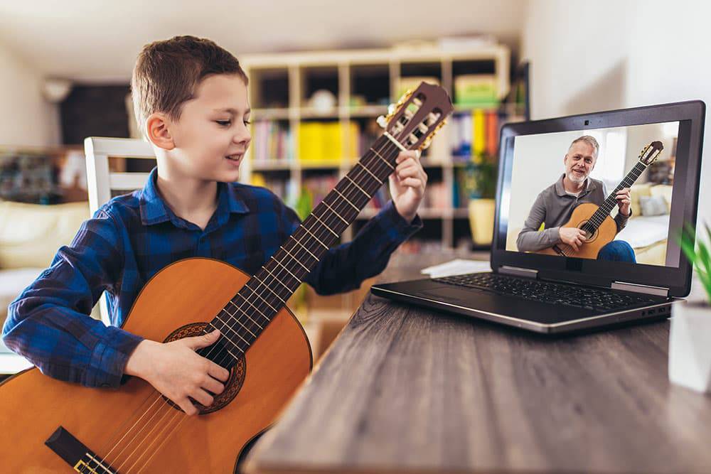 Young boy with guitar looking at laptop with man and guitar online music lesson