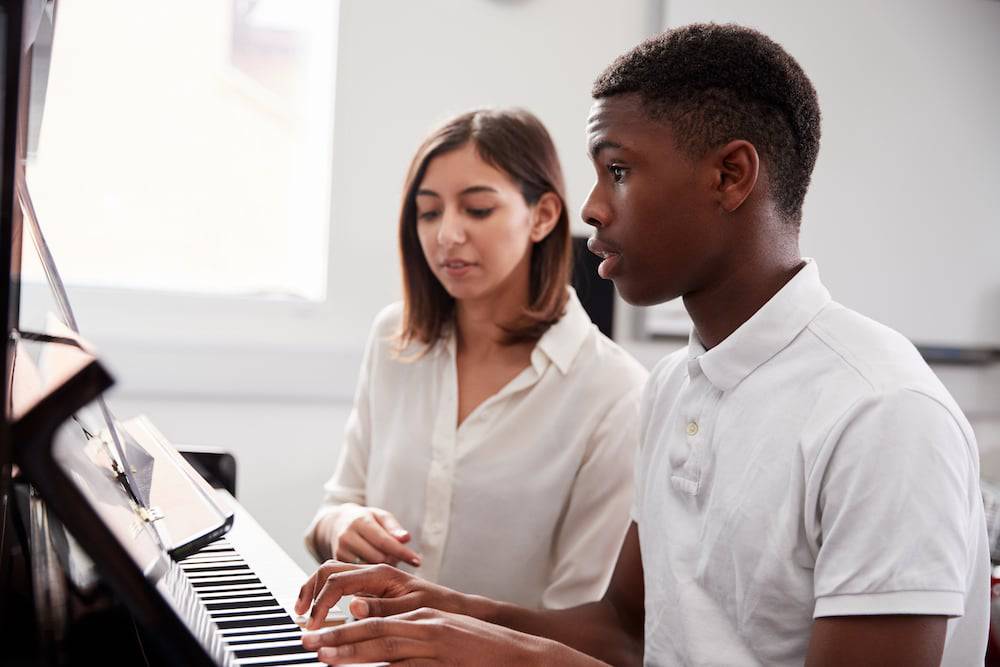 A young man takes private music lessons from a piano teacher