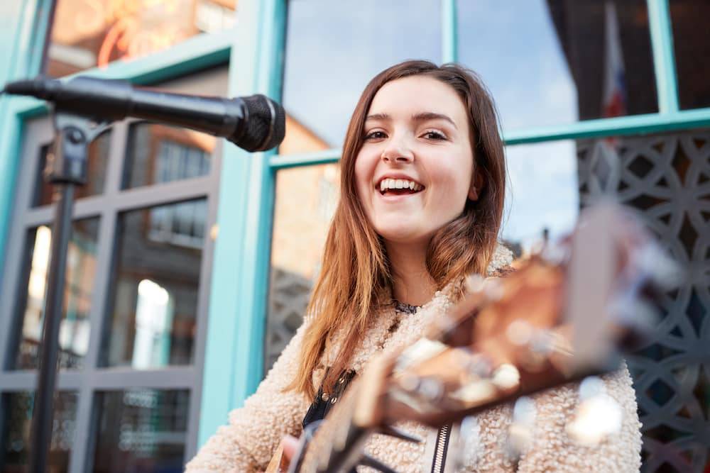 A young woman plays her guitar outdoors during a performance 