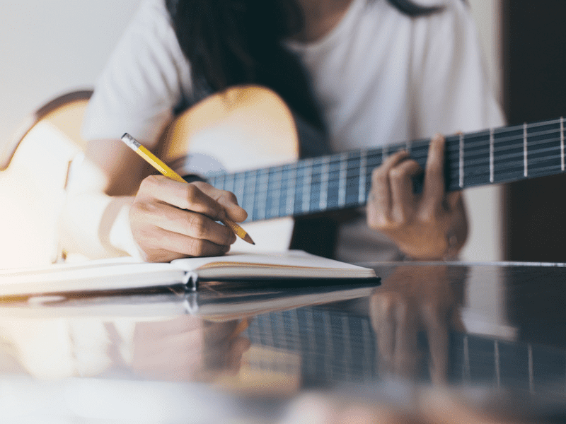 A young woman sits with her guitar and writes music