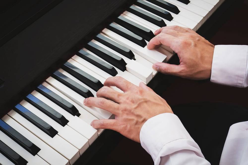 A man's hands are on the keys of a piano as he prepares to play.