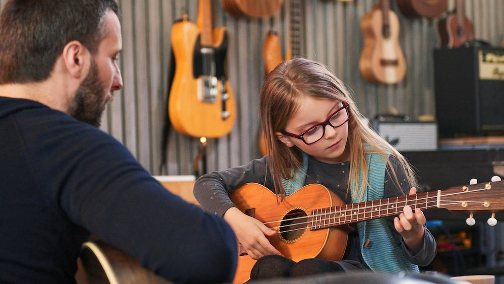 A man teaches a girl how to play guitar.